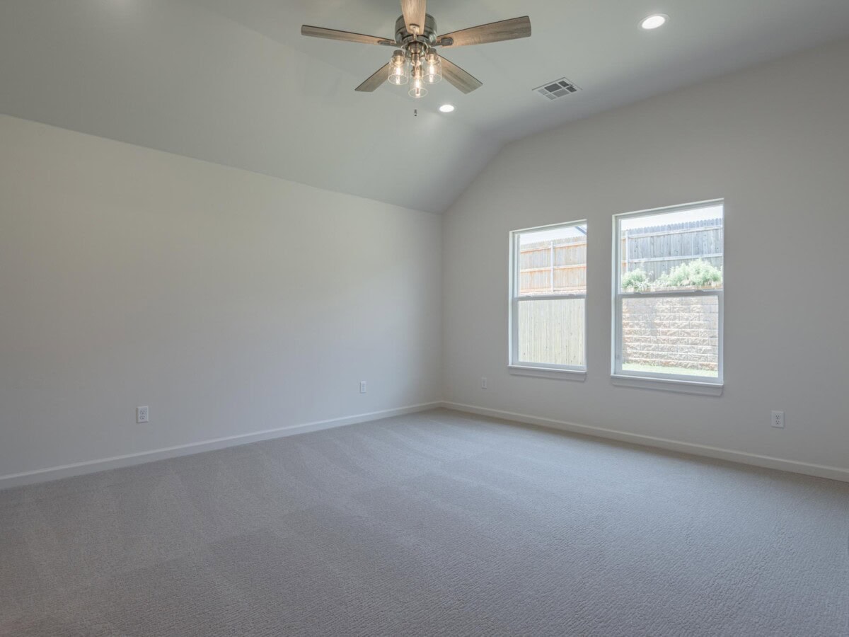 A large empty room with a ceiling fan and windows