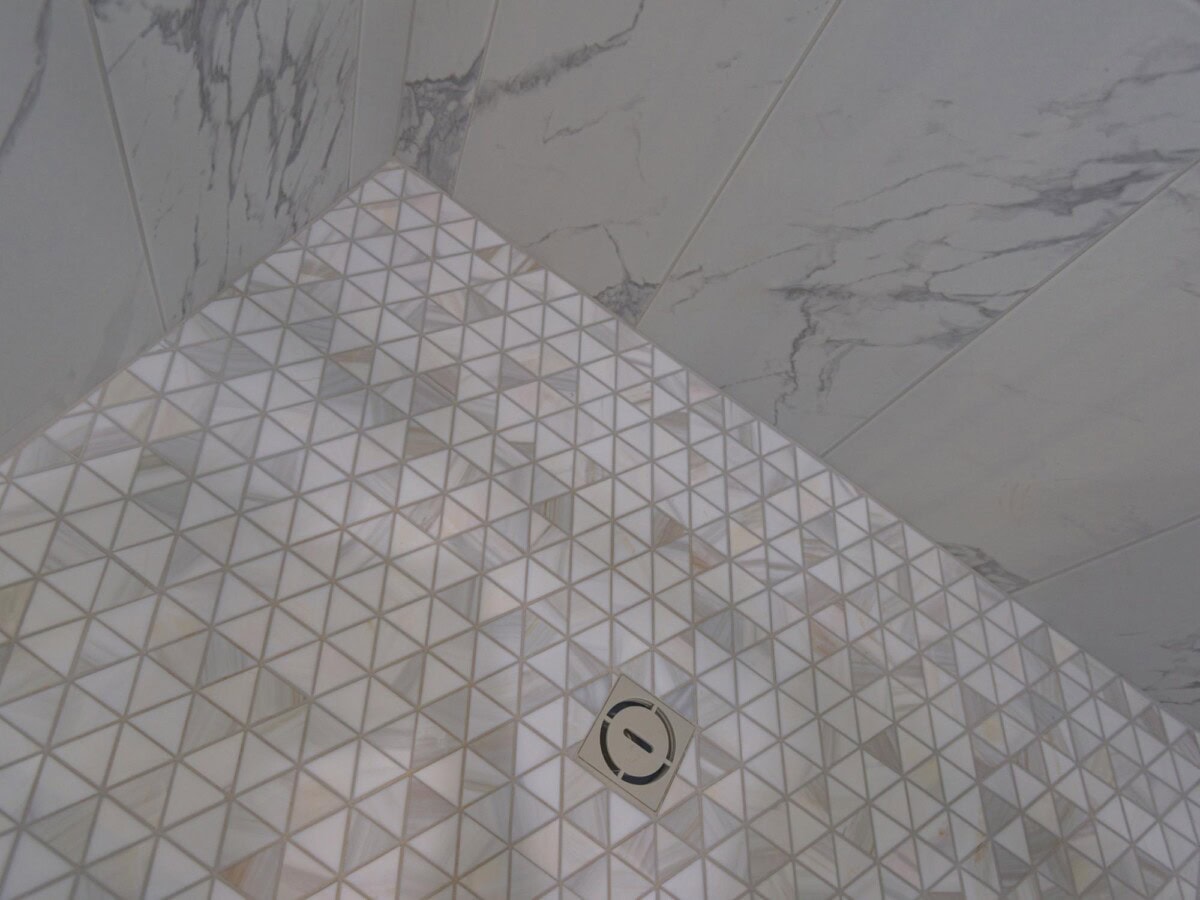 A shower with a white tile floor and a white marble wall
