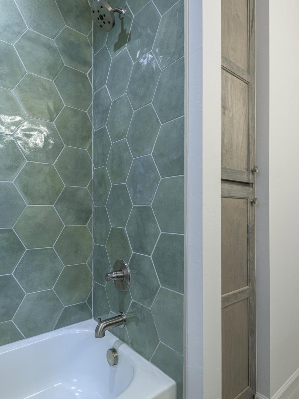 A bathroom with a green tile wall and a white tub