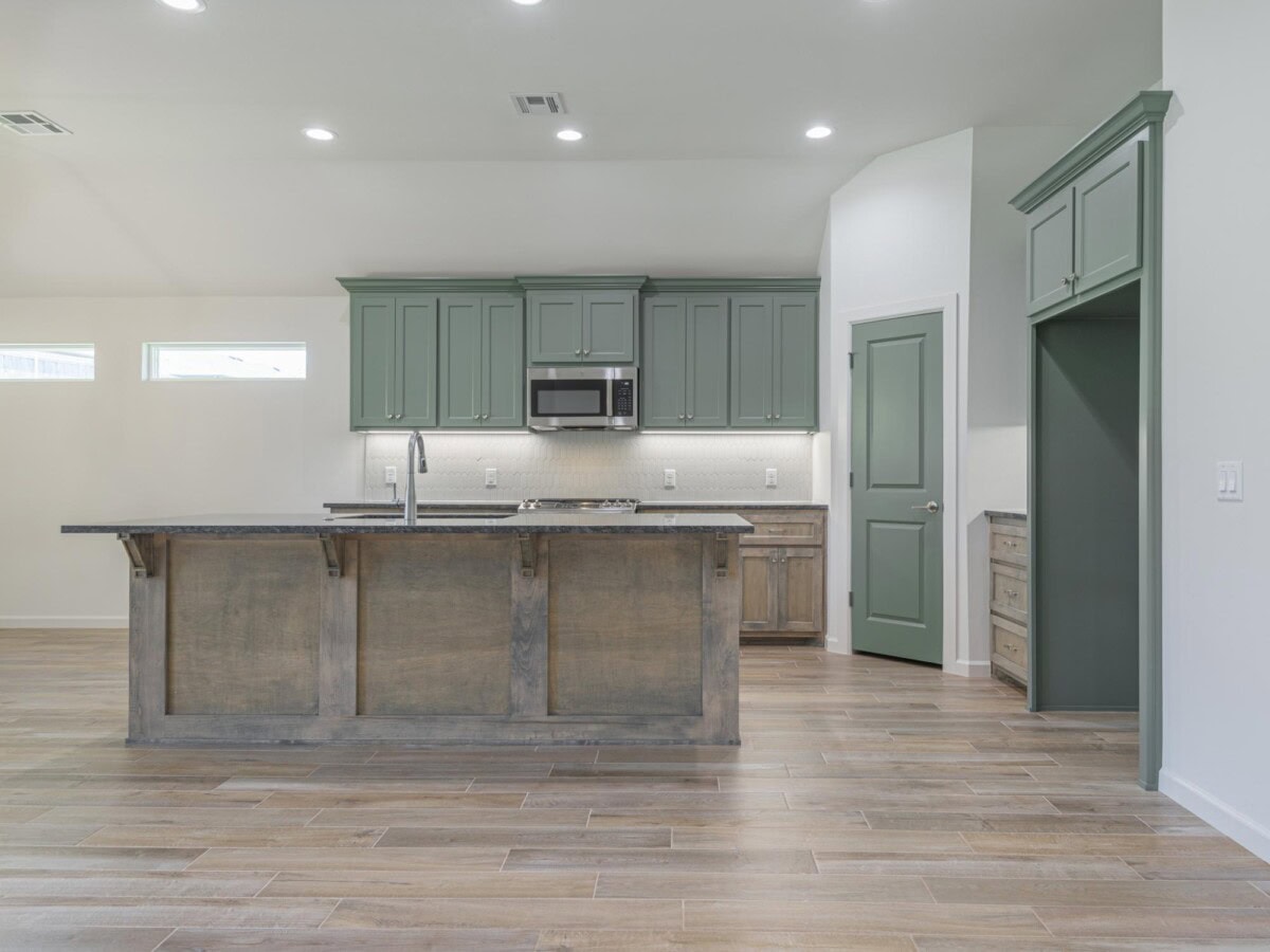 A kitchen with green cabinets and wood floors