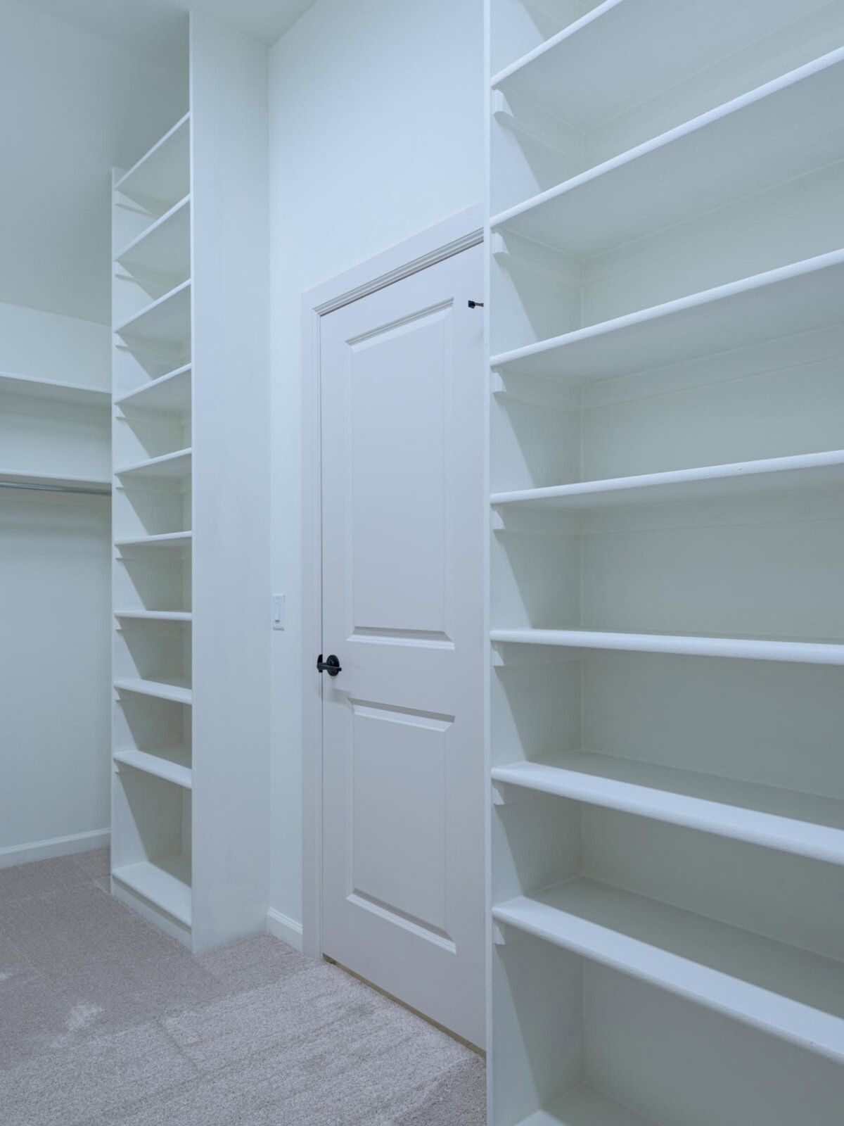 A walk in closet with white shelves and a door