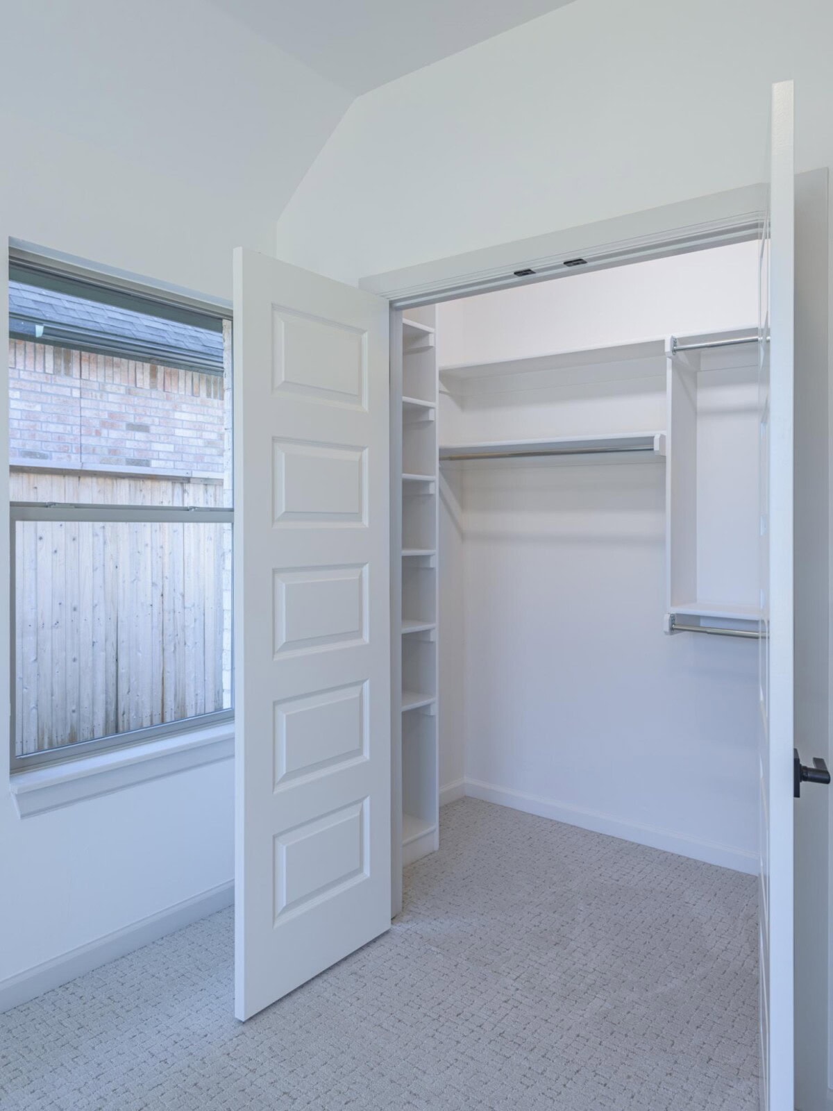 A white closet with open doors and a window